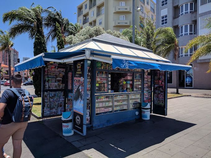 Un hombre con una mochila pasa junto a un quiosco con un toldo azul.