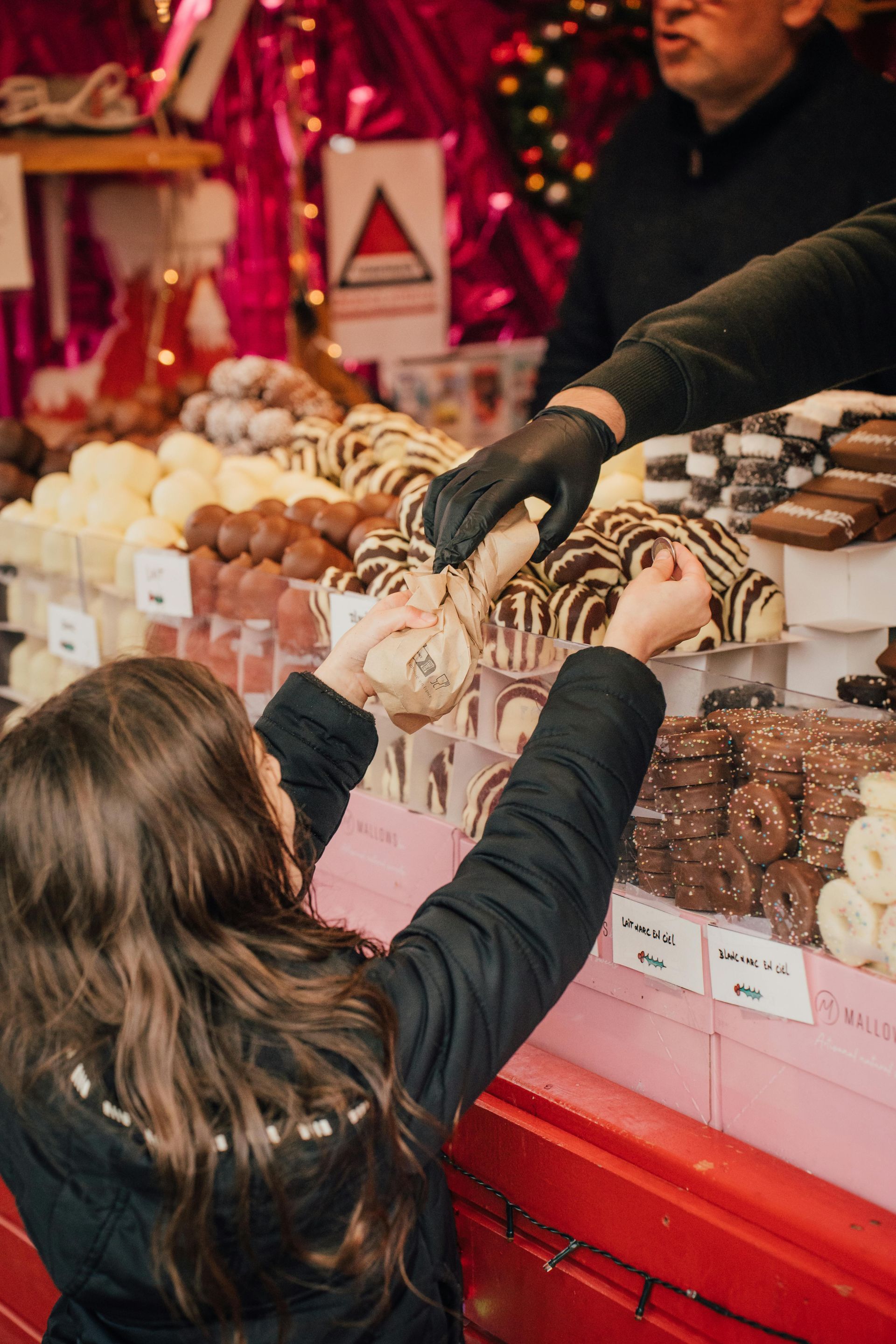 Una niña pequeña está tratando de alcanzar un trozo de chocolate en un puesto de dulces.