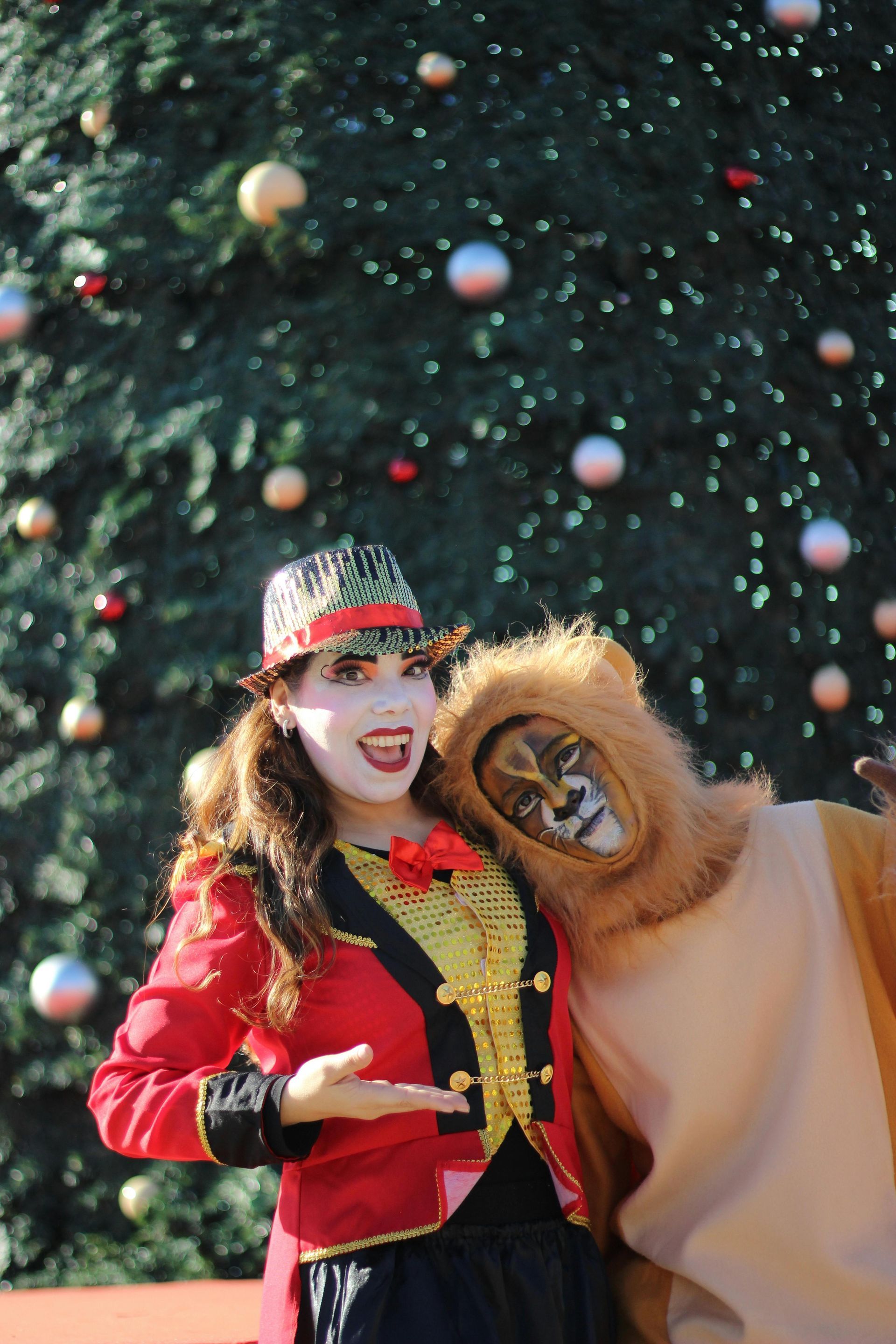 Una mujer disfrazada de circo y un hombre disfrazado de león posan frente a un árbol de Navidad.