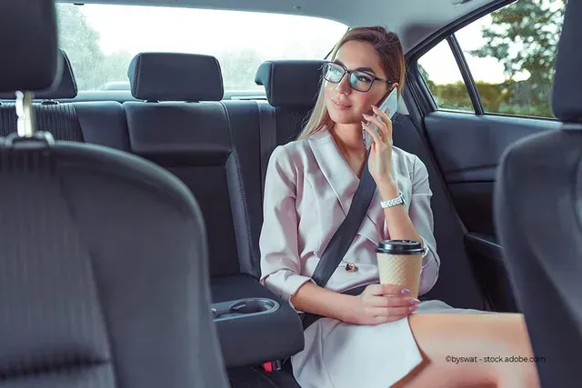 Eine junge Frau auf der Rückbank eines Taxis mit Kaffeebecher und Smartphone in der Hand
