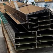 Des piles de profilés métalliques noirs et brillants, probablement destinés à la construction, sur une palette en bois.