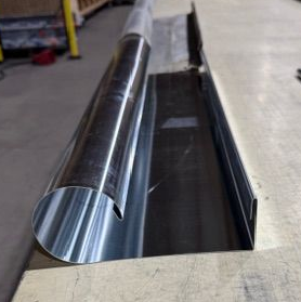 Éléments en tôle : tube roulé et profilé en U, argentés, sur une surface en bois.