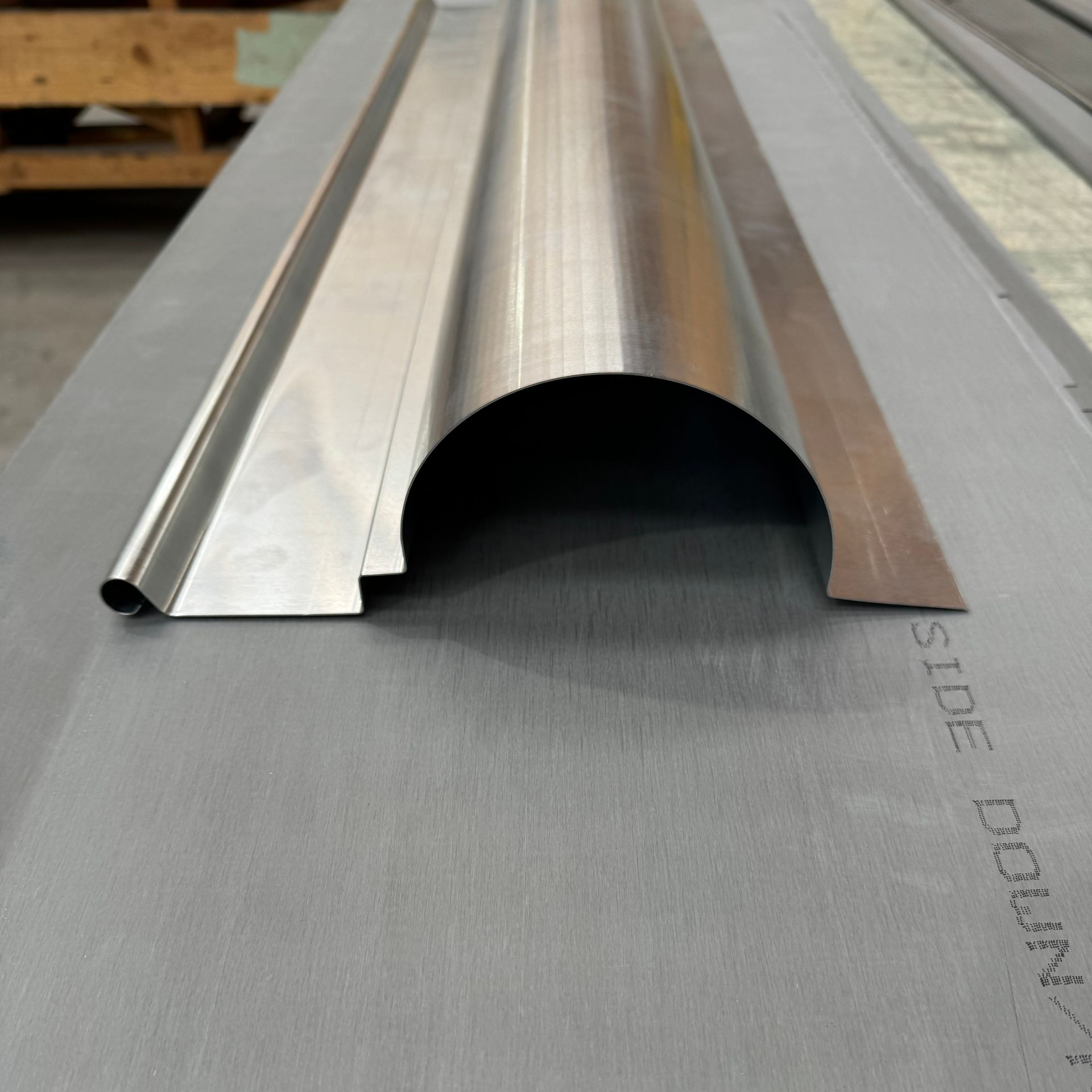 Élément de toiture métallique avec un canal incurvé, reposant sur une feuille de matériau de toiture gris.