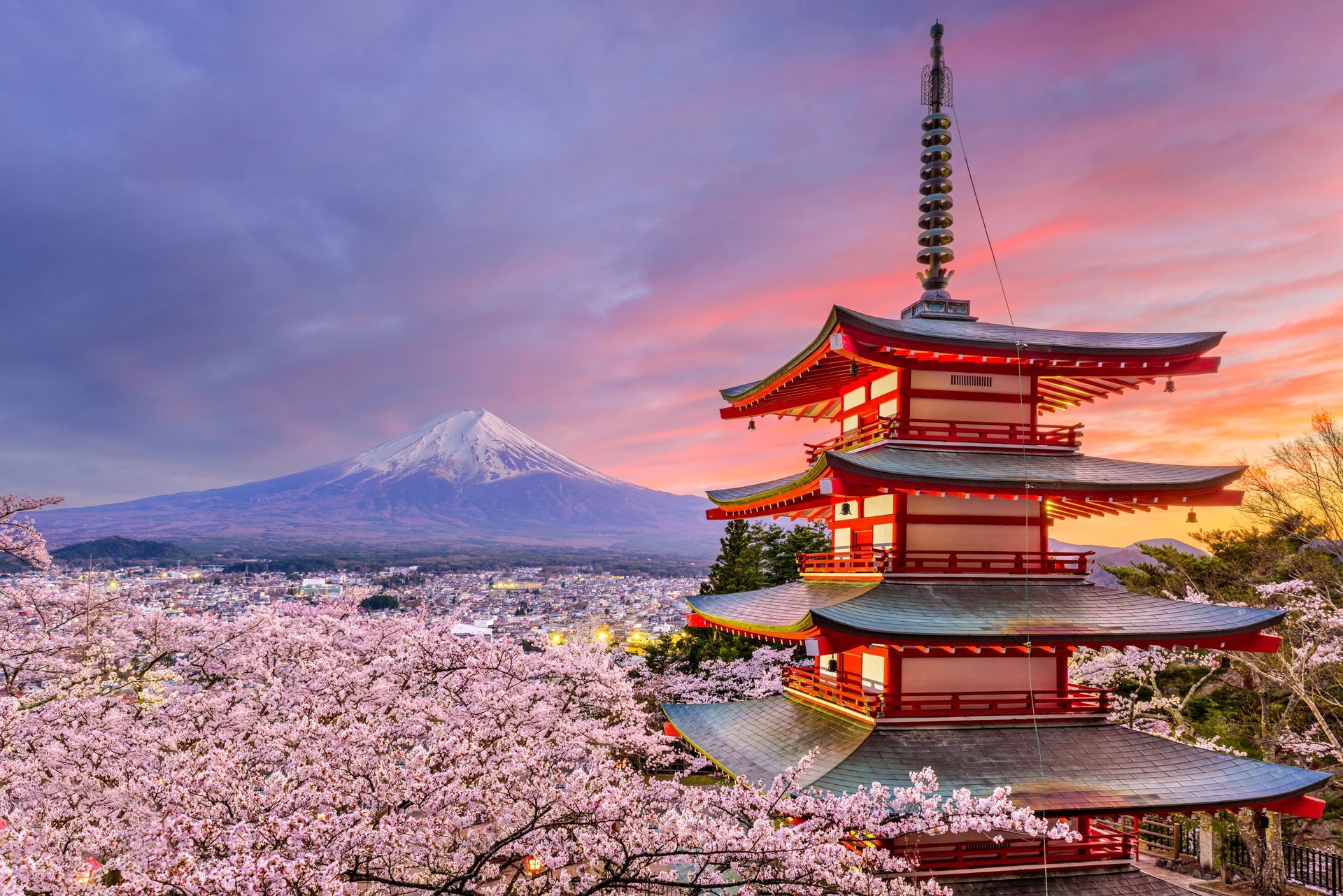 A pagoda with a mountain in the background and cherry blossoms in the foreground.