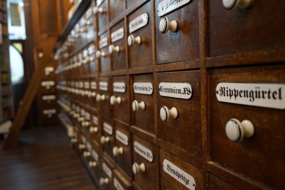 Eine Reihe hölzerner Schubladen mit weissen Etiketten, wahrscheinlich zur Aufbewahrung in einer Apotheke oder Bibliothek.