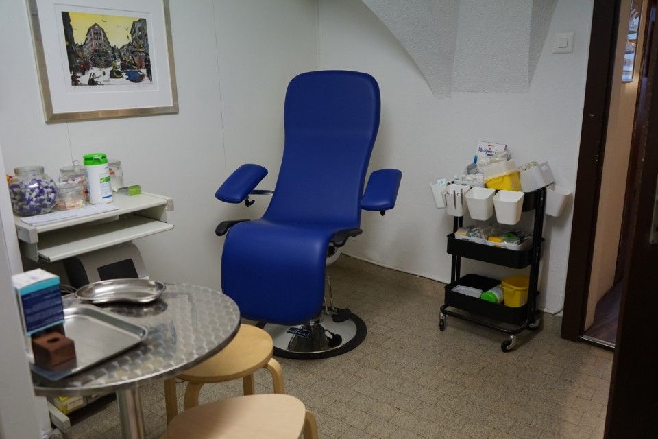 Ein Behandlungsraum mit einem blauen Stuhl, einem kleinen Tisch und Verbandsmaterial.