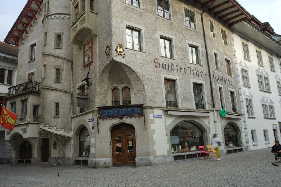 Ein mehrstöckiges, helles Gebäude mit einem Eckturm und einem Bogeneingang. Auf dem Schild steht „Sutterrich-Boutique“.