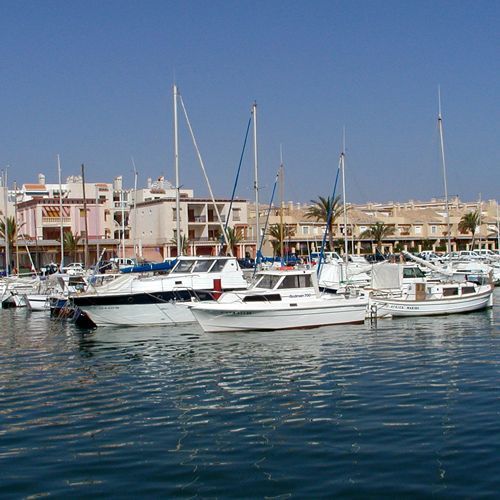 Barcos atracados en un puerto con edificios al fondo bajo un cielo azul.