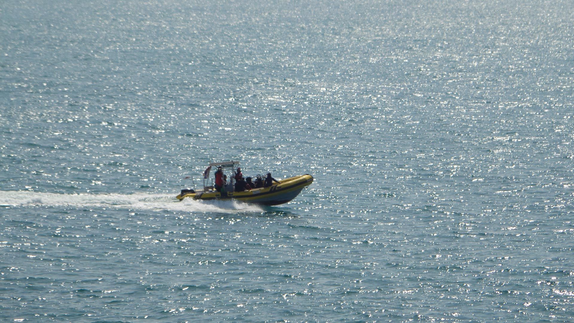 Bote inflable rígido amarillo en agua cristalina con pasajeros.