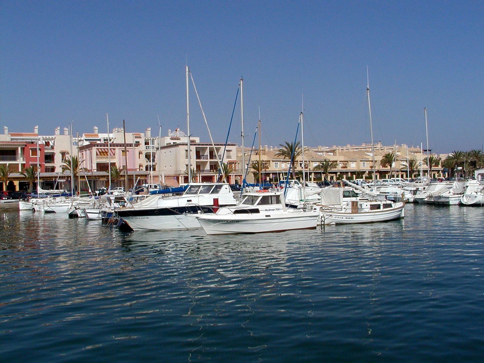Barcos atracados en un puerto con edificios al fondo bajo un cielo azul claro.