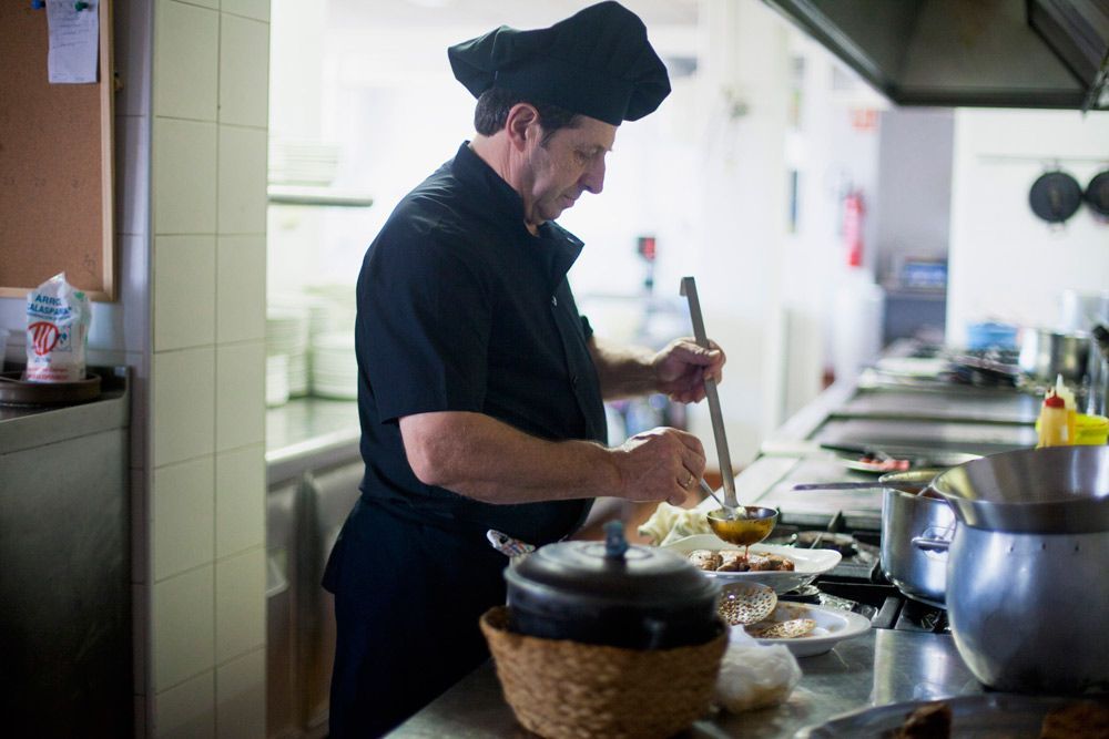 Chef revolviendo comida en la cocina de un restaurante, vistiendo un gorro y uniforme de chef negro.