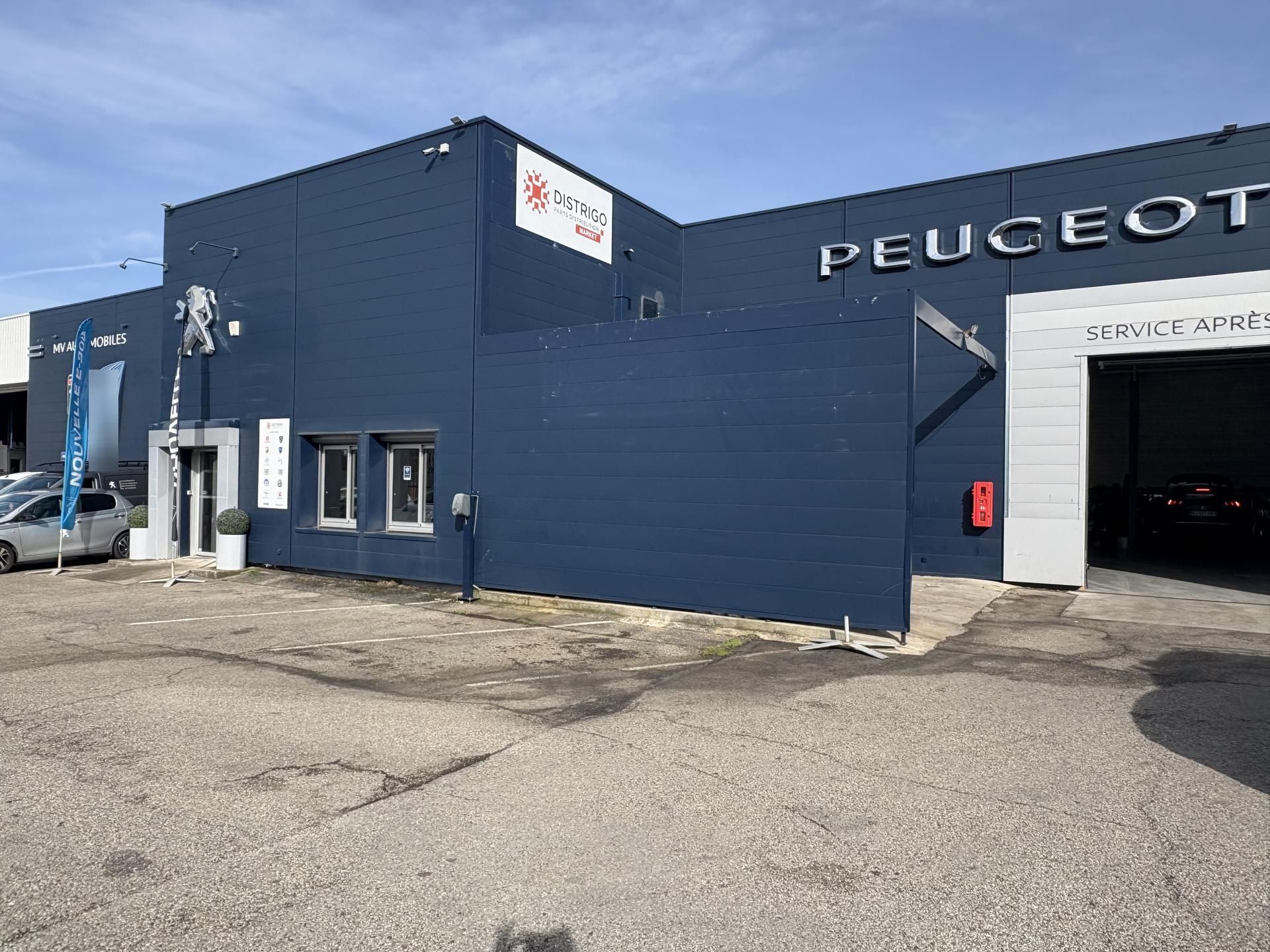 Bâtiment bleu de la concession Peugeot avec une entrée d'atelier sous un ciel dégagé.