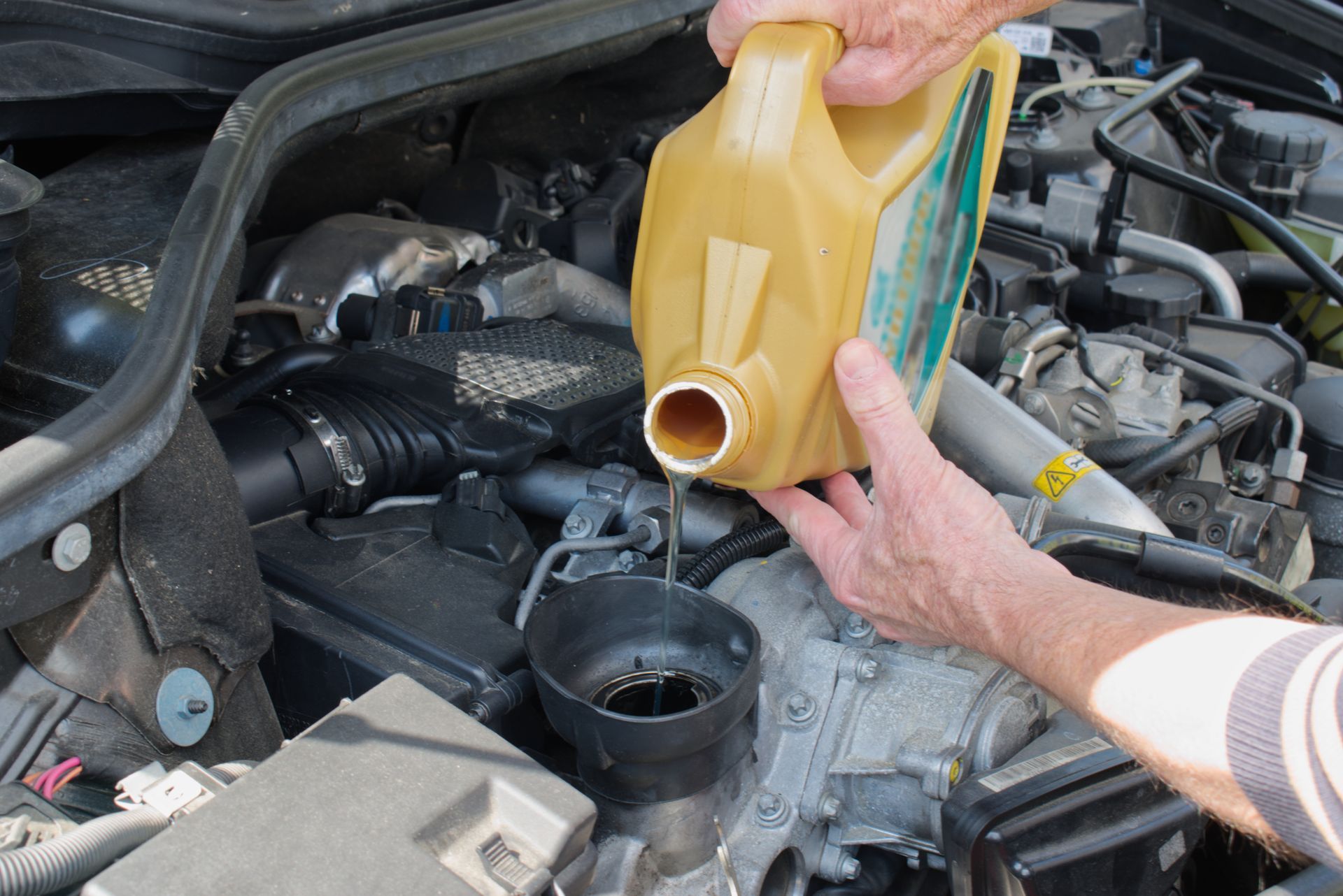 Une personne verse un liquide jaune dans le compartiment moteur d'une voiture à partir d'un récipient.