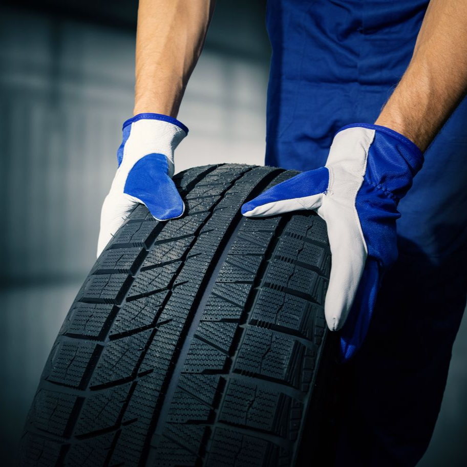 Mécanicien en gants bleus tenant un pneu de voiture en gros plan.