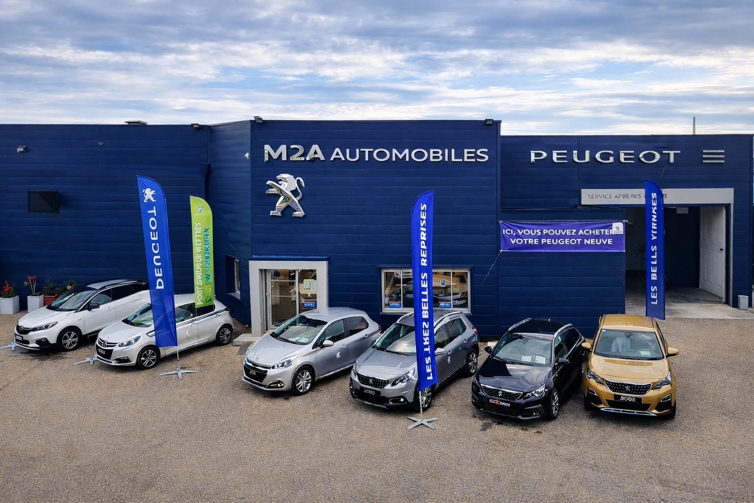 Extérieur d'une concession Peugeot avec plusieurs voitures garées et des drapeaux bleus devant.