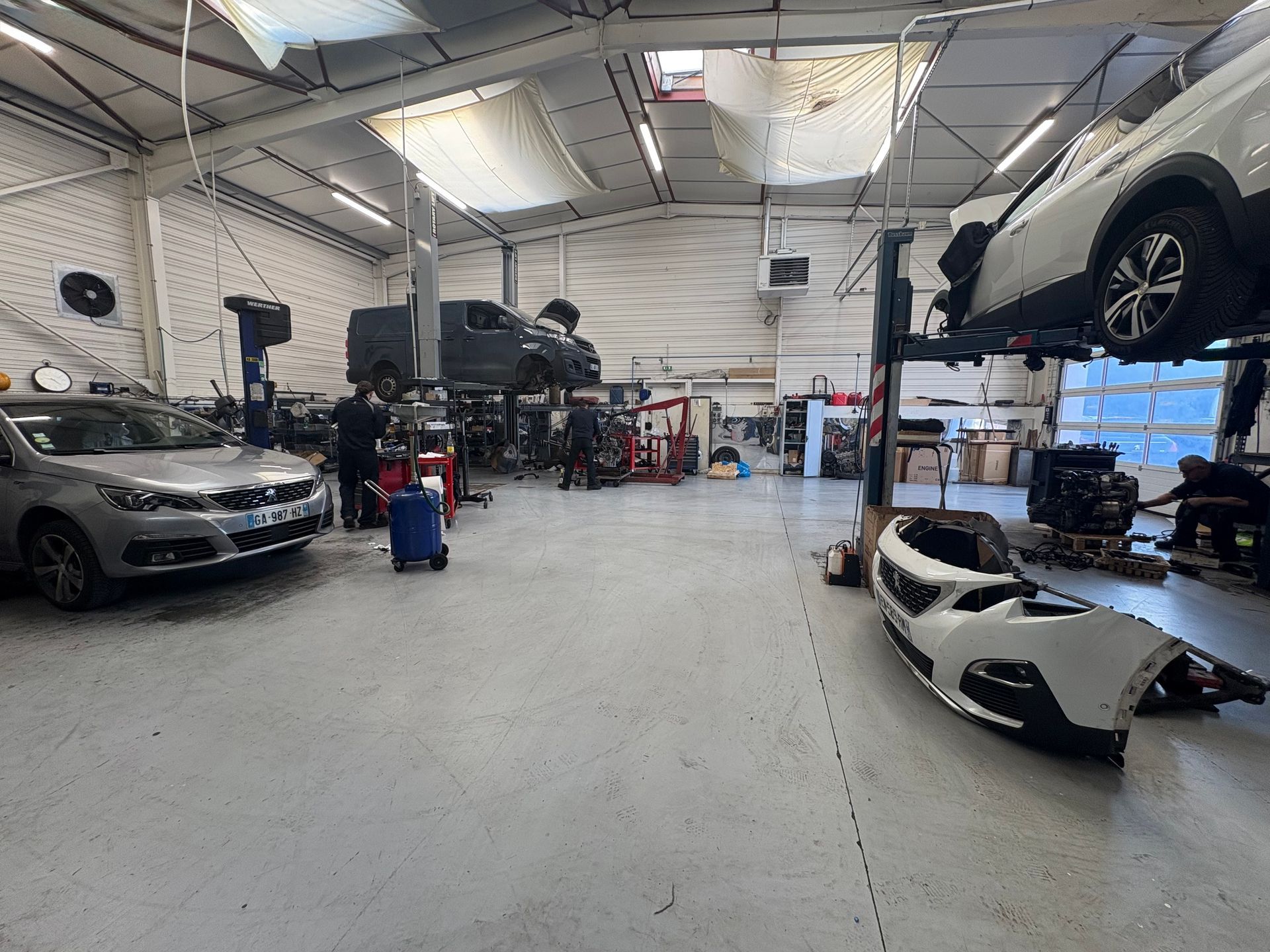Atelier de réparation automobile avec plusieurs voitures sur des ponts élévateurs et dans des baies, intérieur de garage industriel lumineux