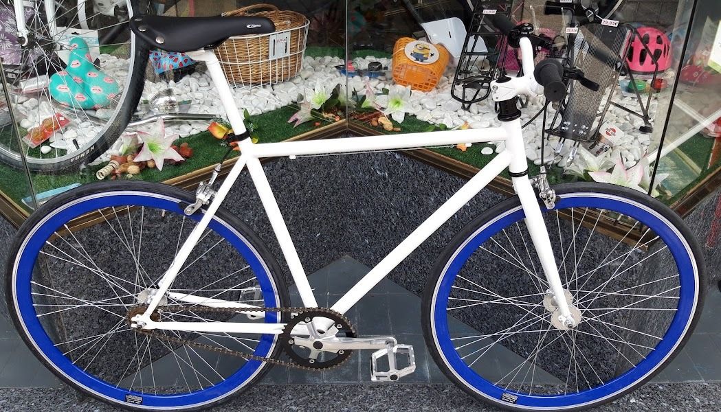 Una bicicleta blanca con ruedas azules está estacionada frente al escaparate de una tienda.