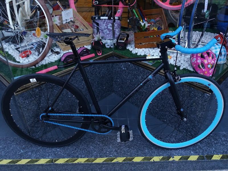 Una bicicleta negra con ruedas azules está estacionada en la acera
