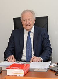 Ein Mann in Anzug und Krawatte sitzt an einem Schreibtisch.