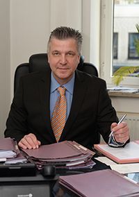 Ein Mann in Anzug und Krawatte sitzt an einem Schreibtisch und hält einen Stift in der Hand.