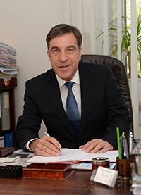 Ein Mann in Anzug und Krawatte sitzt an einem Schreibtisch und schreibt auf ein Blatt Papier.