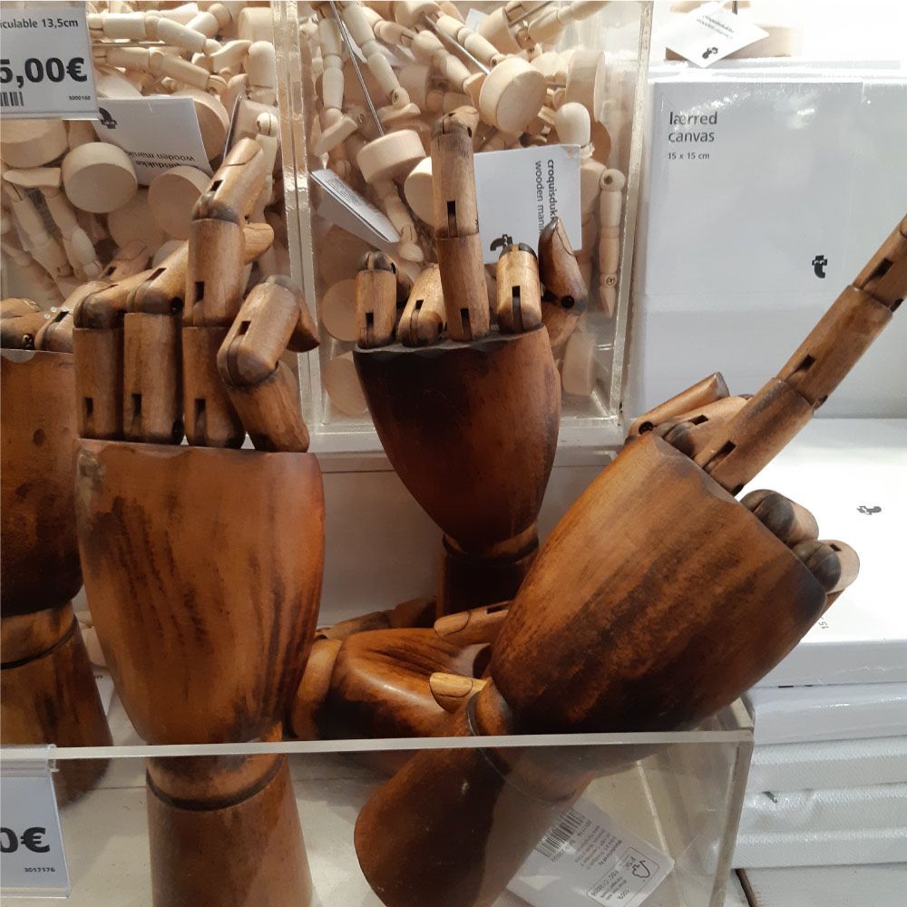 Manos de artista de madera en la vitrina de una tienda, una apuntando, otras abiertas, junto a más manos en un recipiente transparente.