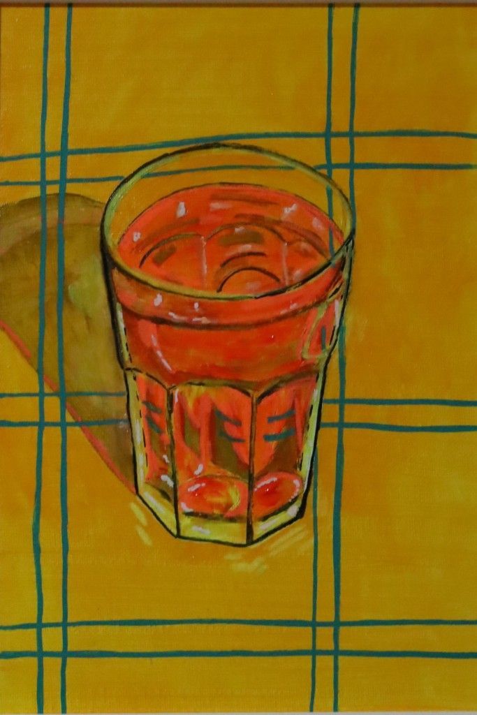 Vaso de líquido rojizo sobre un mantel amarillo con líneas verdes.