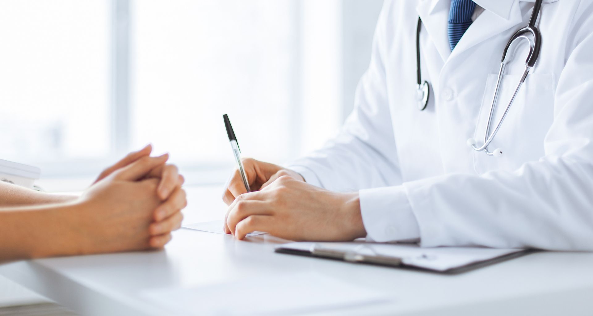 Un médecin prend des notes pendant qu'il parle avec un patient à un bureau dans une clinique lumineuse.
