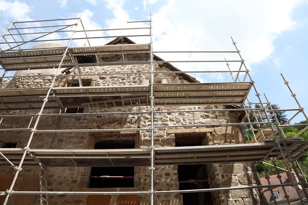 Des échafaudages recouvrent l'extérieur d'un bâtiment en pierre en rénovation, sur fond de ciel bleu éclatant.
