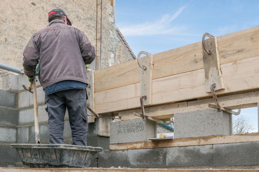 Une personne se tient sur un chantier de construction, en train d'édifier une structure en bois sur des blocs de béton.