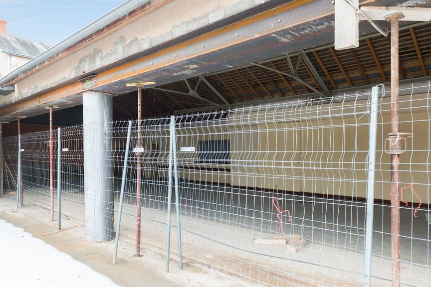 Chantier de construction montrant la structure ouverte d'un bâtiment soutenue par des étais métalliques et une grille en treillis d'acier renforcé.