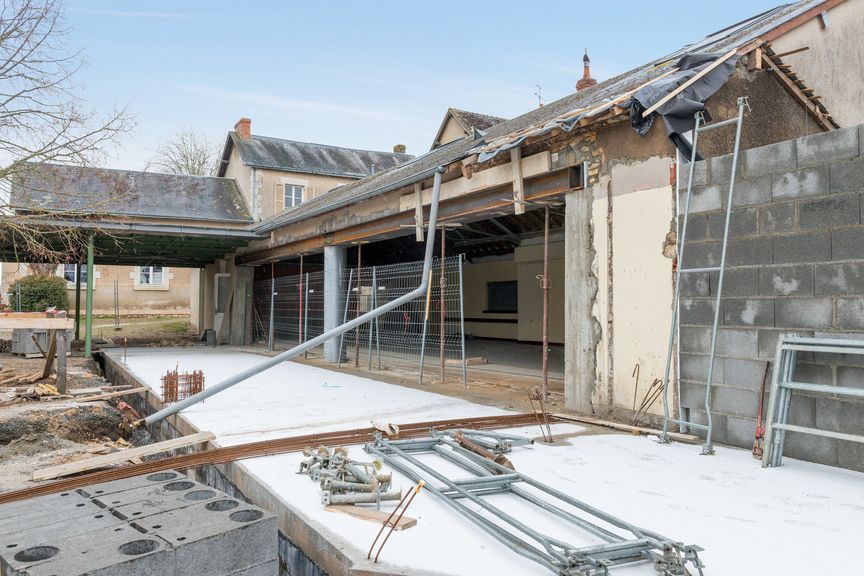 Chantier de construction montrant la rénovation d'un bâtiment avec des poutres de toiture étayées, un sol en béton et des échafaudages métalliques.