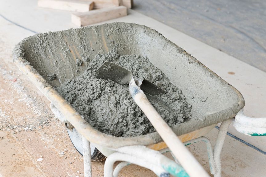 Une brouette remplie de béton frais, avec une pelle à l'intérieur, sur un chantier.