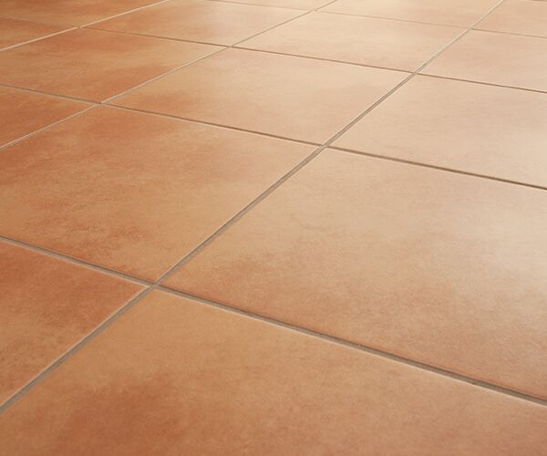 Gros plan sur des carreaux de sol carrés couleur terre cuite aux joints fins, vus d'un angle légèrement oblique.