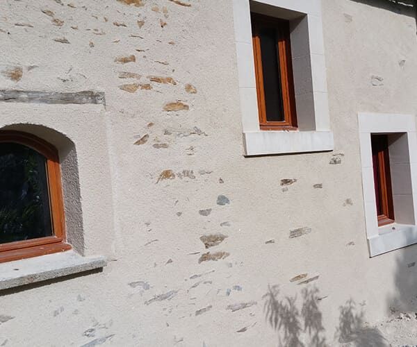 Mur en stuc texturé beige orné de trois fenêtres rectangulaires aux cadres en bois chaleureux et aux finitions en pierre claire.