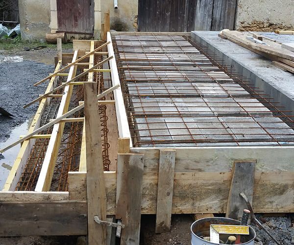 Coffrage en bois pour une fondation en béton, comprenant un treillis d'armature en acier et des blocs de remplissage en briques, sur un chantier extérieur.