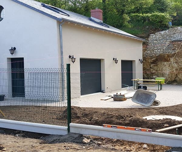 Une maison à l'extérieur blanc et crème, avec une porte de garage grise et une cour partiellement pavée en construction.
