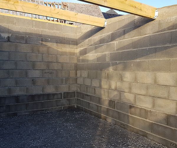 Angle intérieur d'une structure en construction avec des murs en blocs de béton gris et des poutres de soutien en bois au-dessus.