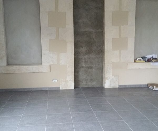 Un intérieur moderne avec des sols carrelés gris, des murs beiges ornés de piliers en pierre et un panneau central en pierre grise.