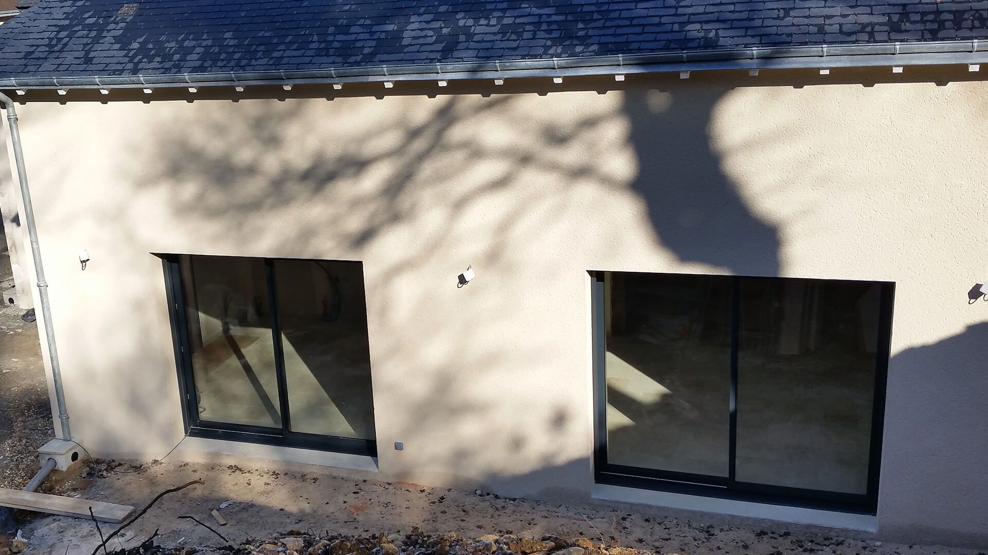 Vue extérieure d'un mur d'immeuble en stuc clair, comportant deux portes coulissantes en verre à cadre foncé sous un toit.