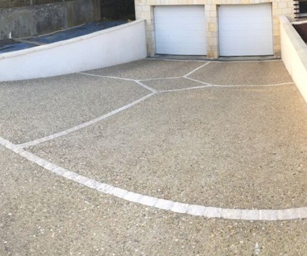 Une allée résidentielle en béton désactivé avec des bordures décoratives en pierre blanche et un garage double.