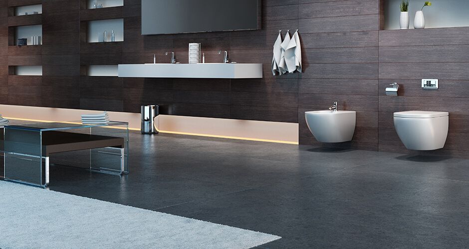 Une salle de bains moderne avec un long meuble-lavabo suspendu, des murs lambrissés de bois foncé et des toilettes et un bidet suspendus.