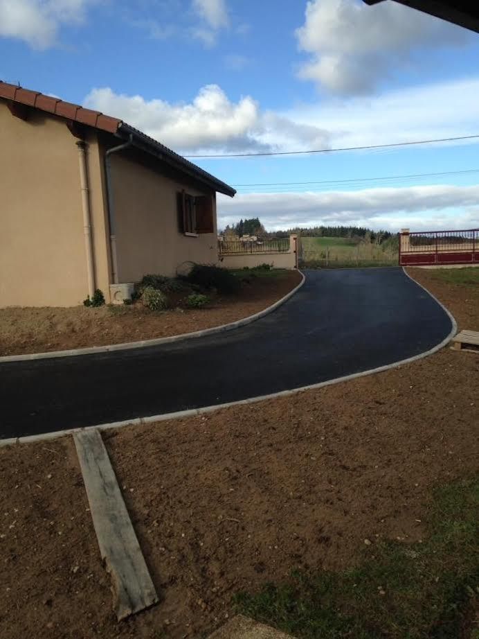 Allée noire incurvée longeant une maison beige, menant à une route sous un ciel nuageux.