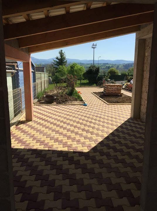 Terrasse couverte avec sol carrelé à motifs, plantes en pot et vue ensoleillée sur la montagne au-delà du jardin