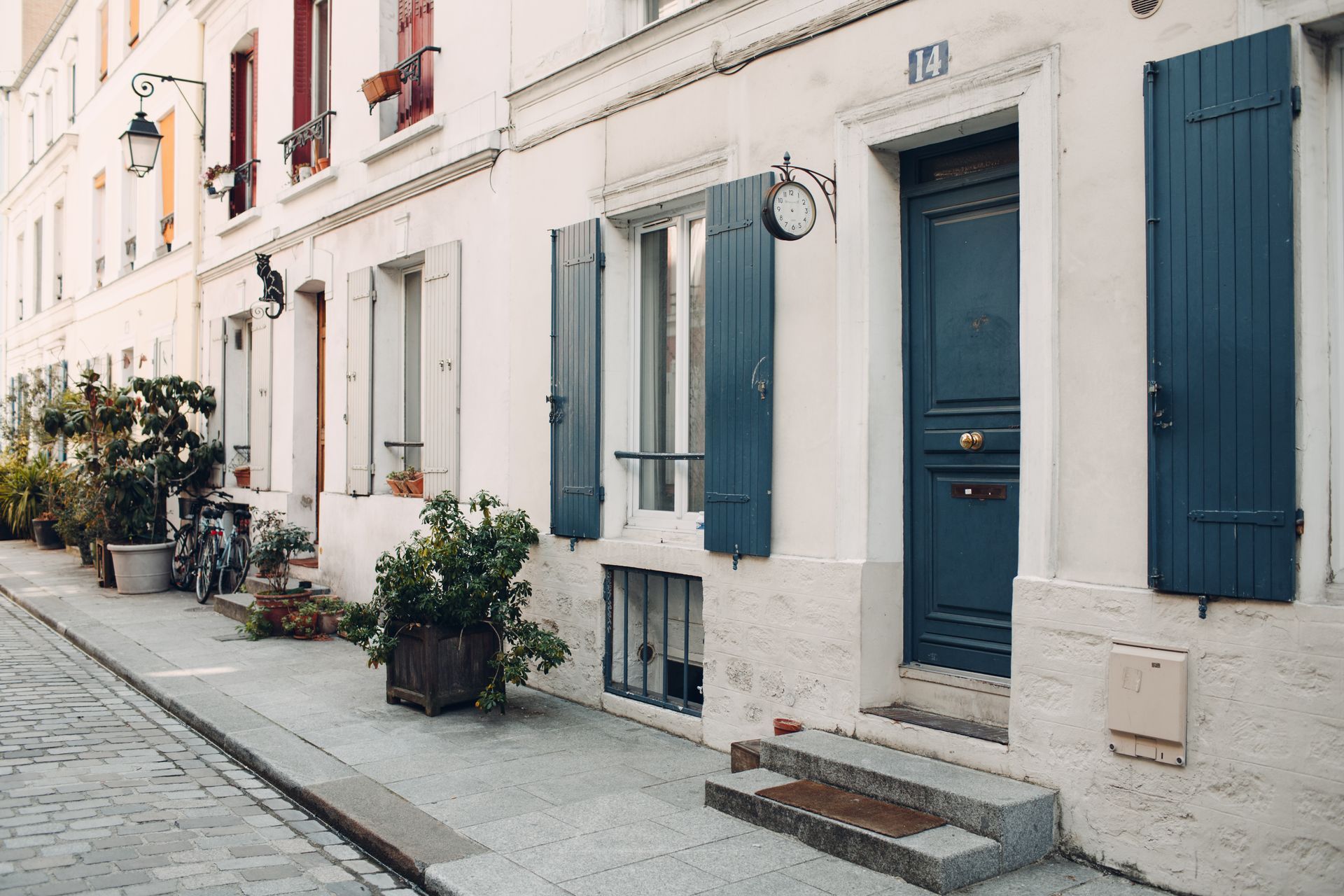 Rue pavée étroite bordée de maisons de ville blanches, de volets bleus et de plantes en pot