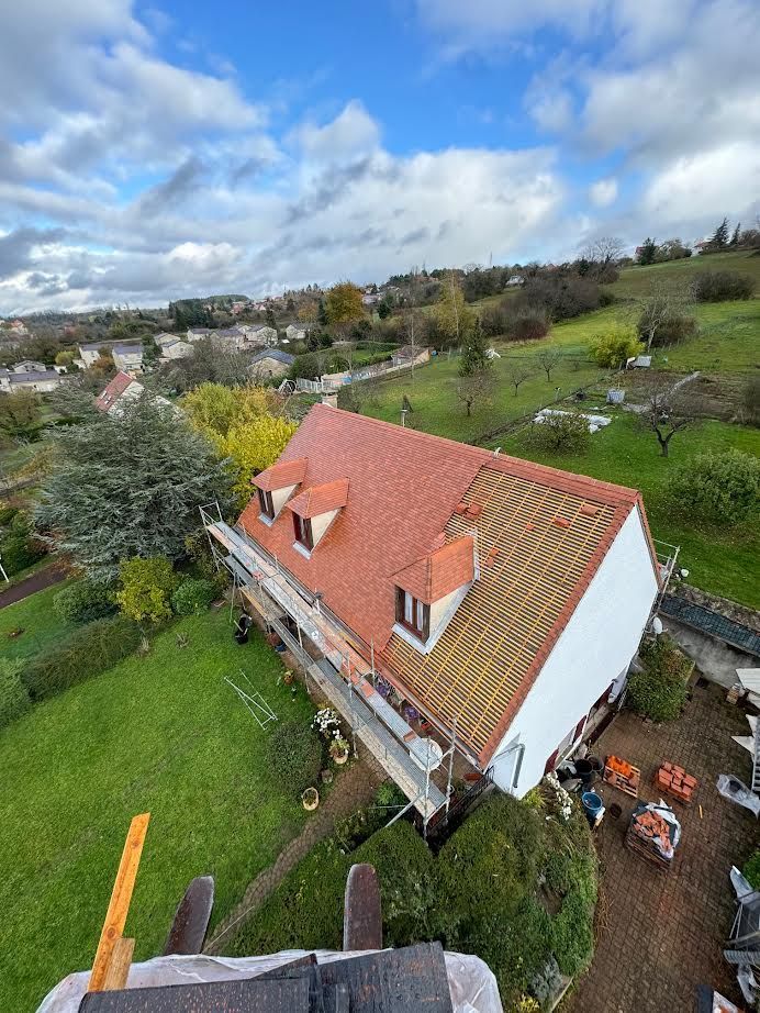 Vue aérienne d'une maison au toit rouge avec un jardin verdoyant dans un quartier rural sous un ciel nuageux