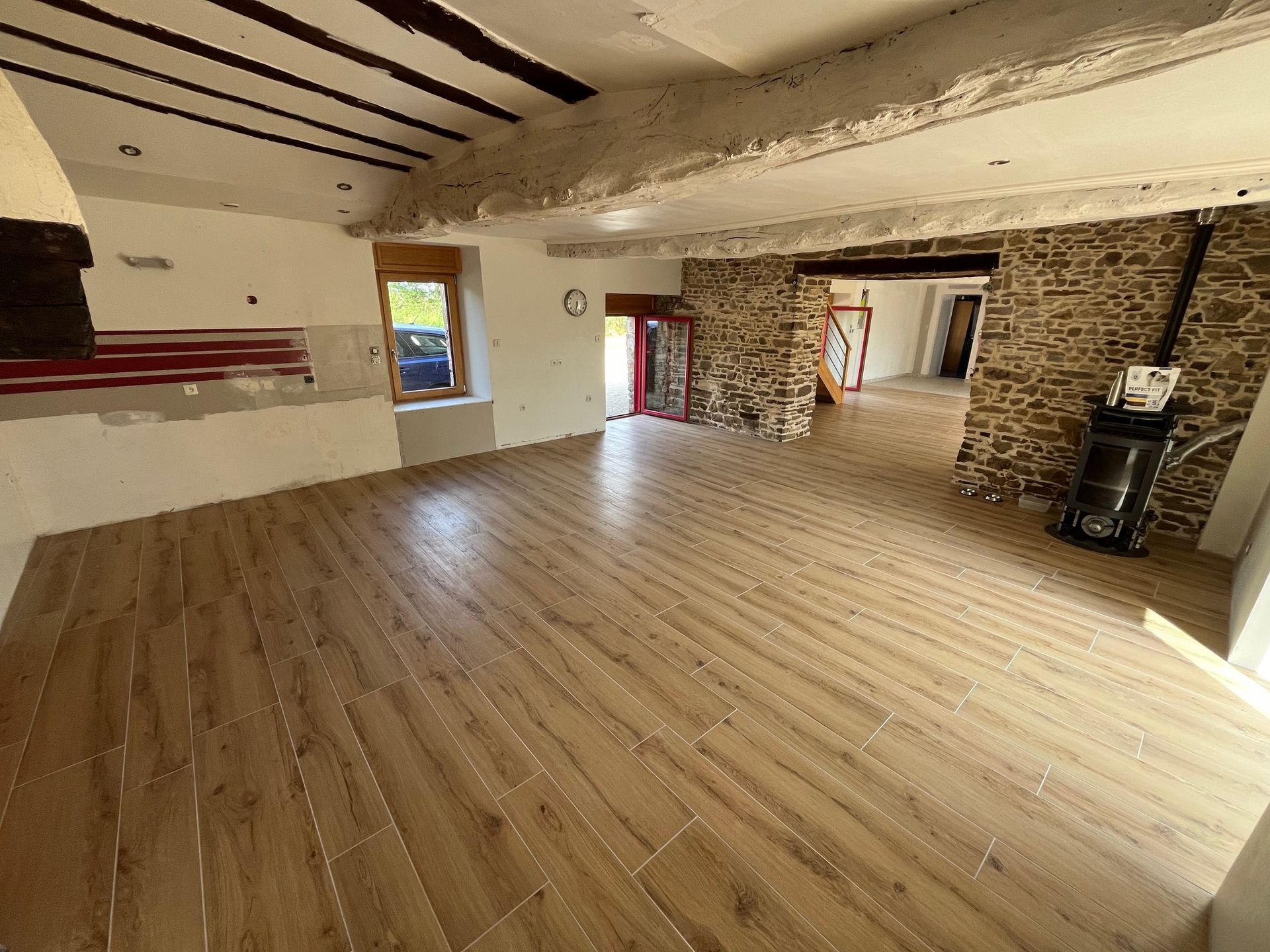 Pièce rustique vide avec parquet, poutres apparentes et murs en pierre.