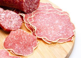 Rebanadas de salami están en una tabla de cortar de madera.