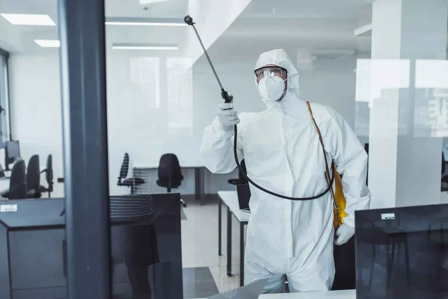 Un hombre con un traje de protección está desinfectando una oficina con un pulverizador.