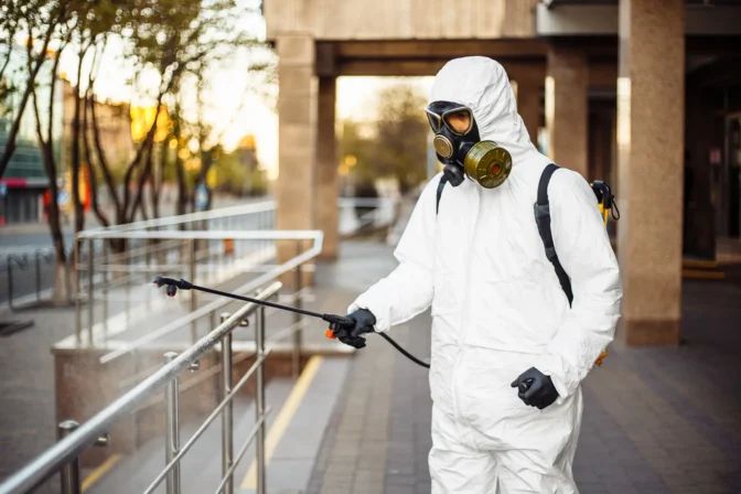 Un hombre con un traje de protección está rociando una barandilla con un pulverizador.